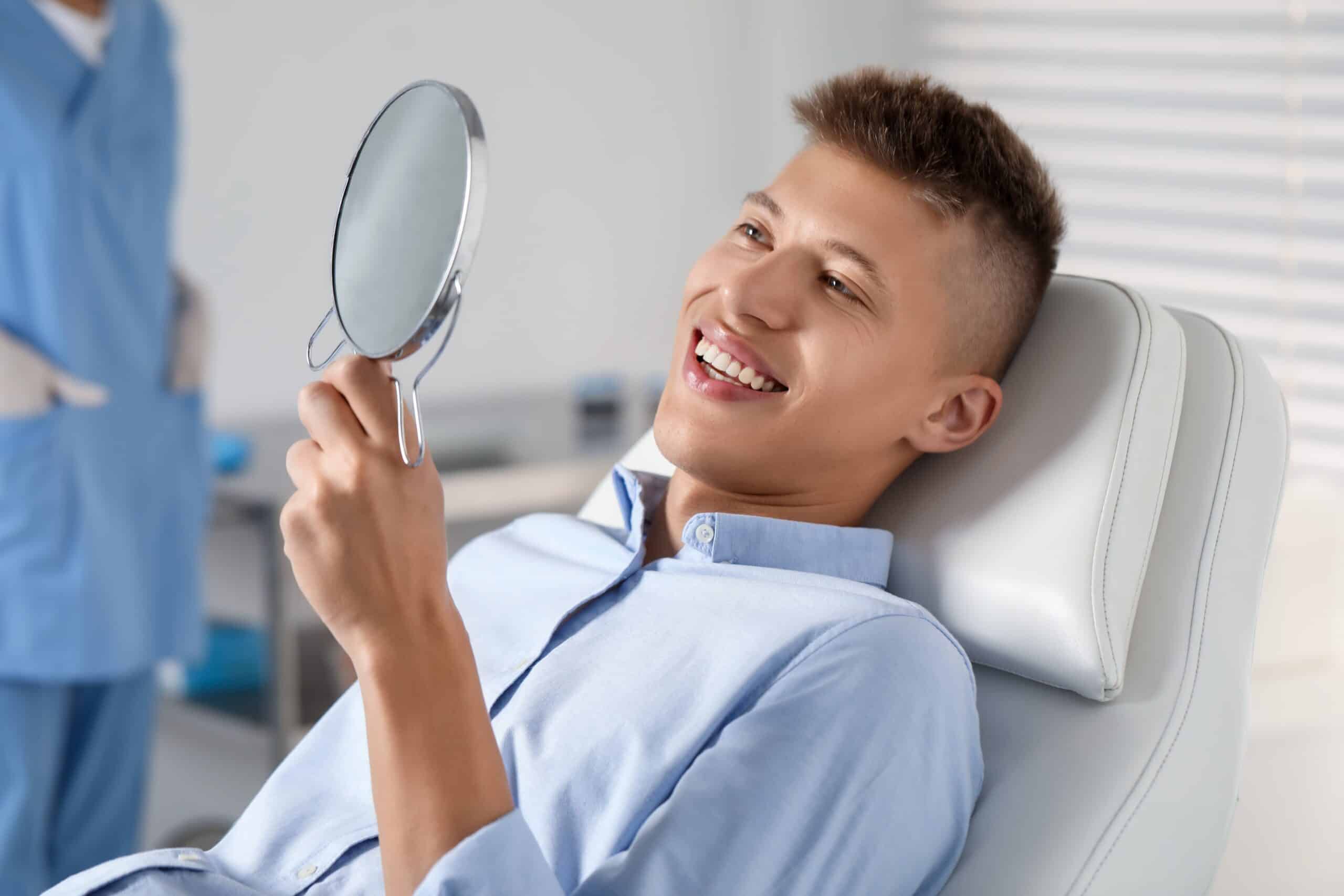 Happy,Young,Man,With,Mirror,In,Clinic,,Closeup.,Dental,Veneers
